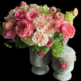 Lush arrangement of pink and peach roses, ranunculus, and hydrangeas in two rustic stone urn vases.