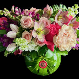 Mixed bouquet of pink roses, tulips, and hellebores in a green vase