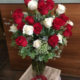 Red and white roses arranged in a clear glass vase with a red ribbon.