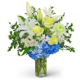 White lilies, yellow roses, and blue hydrangeas in a clear glass vase