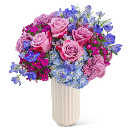 Bouquet of pink roses, blue hydrangeas, and purple flowers in a white vase