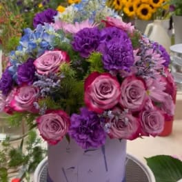 Round bouquet of pink and purple flowers in a lavender hat box