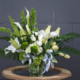 White lilies and green blooms arranged in a glass vase with a ribbon