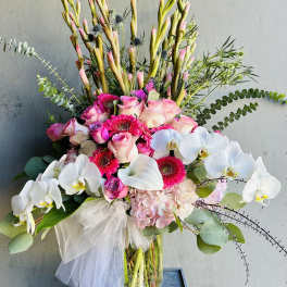 Tall bouquet of pink roses, white orchids, and gerbera daisies in a glass vase