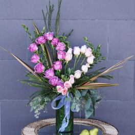 Pink and white roses in a tall green vase with ribbon