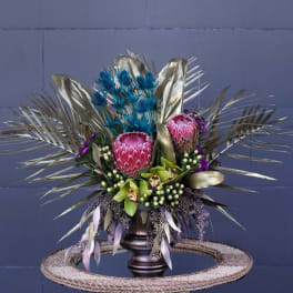 Tropical bouquet with pink protea and blue thistle in a dark vase