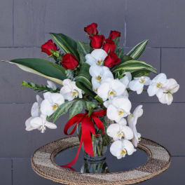 Red roses and white orchids in a glass vase with a red ribbon