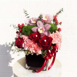 Pink orchids and red roses in a black vase with a red ribbon