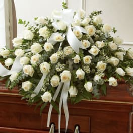 White rose casket spray with white ribbon on a wooden casket