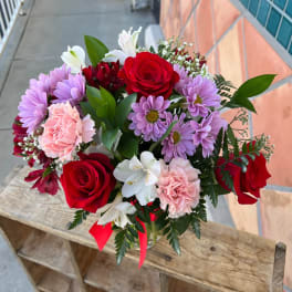 Bouquet of red roses, pink carnations, and purple daisies in a glass vase