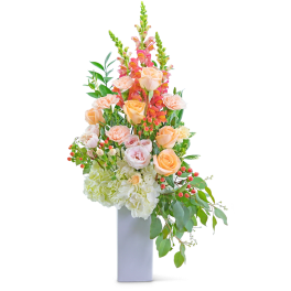 Tall floral arrangement with peach roses, pink snapdragons, and white hydrangeas in a white vase