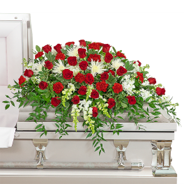 Red roses and white flowers arranged on a white casket