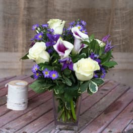 Bouquet of white roses, purple calla lilies, and small purple daisies in a glass vase
