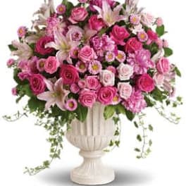 Large pink rose and lily arrangement in an ivory pedestal urn with trailing accents