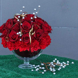 Red roses and carnations in a glass compote with gold ribbon and white berry picks