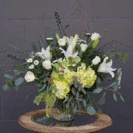White lilies and roses with pale green hydrangeas in a glass vase