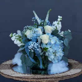 Blue and white floral arrangement in a glass vase on a woven tray