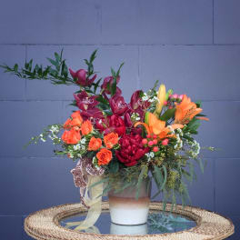 Mixed bouquet with orange lilies, red orchids, and orange roses in a ceramic vase