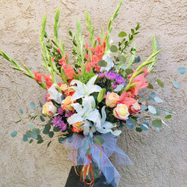Tall mixed bouquet with lilies, roses, and gladiolus in a glass vase
