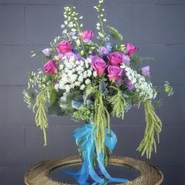 Pink roses and lavender flowers in a glass vase with a blue ribbon