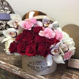 Bouquet of red and pink roses with white orchids in a round box