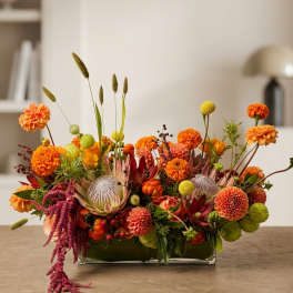 Low rectangular arrangement of orange and yellow flowers in a glass vase