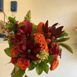 Handheld bouquet of red and orange flowers with green foliage