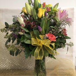 Mixed bouquet of lilies and roses in a glass vase with a yellow bow