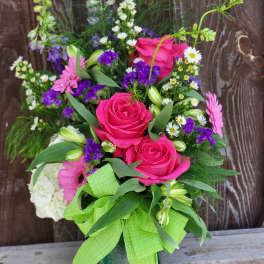 Pink roses and mixed flowers in a glass vase with a green ribbon