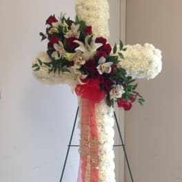 White floral cross on an easel with red roses and orchids