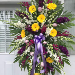Standing floral spray with yellow daisies, purple and white blooms, and a lavender ribbon
