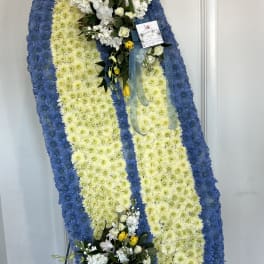 Large oval funeral wreath with blue and white flowers and yellow accents