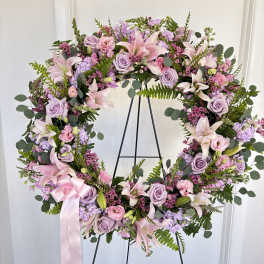 Lavender and pink floral wreath on a black stand with a pink ribbon