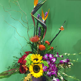 Tropical flower arrangement with sunflowers, orchids, and red roses in a vase