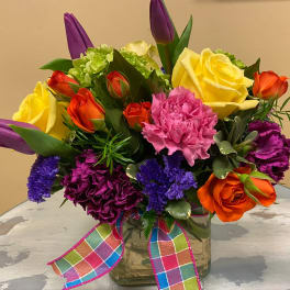 Colorful bouquet of roses, carnations, and tulips in a glass vase with a plaid ribbon