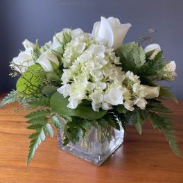 Low arrangement of white roses and hydrangeas in a clear glass cube vase