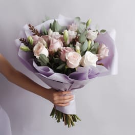 Handheld bouquet of pale pink and white roses wrapped in lavender paper