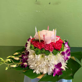Round floral cake with candles, white chrysanthemums, pink blooms, and purple orchids