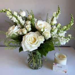 White roses and snapdragons in a glass vase beside a candle
