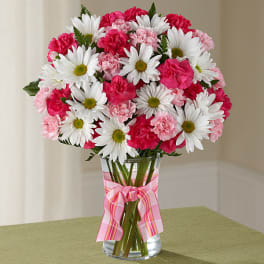 Pink carnations and white daisies in a glass vase with a pink ribbon