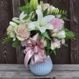Bouquet of white lilies and pale pink roses in a blue vase with a pink ribbon