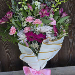 Hand-tied bouquet of pink and white flowers wrapped in white paper with a pink bow.