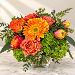 Bright mixed bouquet in a clear glass vase with orange roses and a yellow gerbera daisy