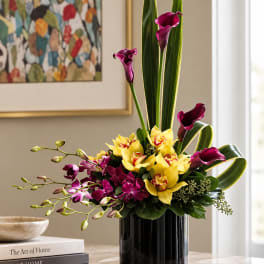 Purple calla lilies and yellow orchids in a black vase