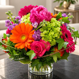 Bright mixed bouquet in a clear glass vase with pink, orange, purple, and green blooms