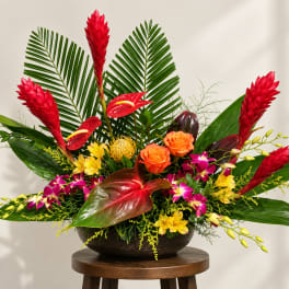 Tropical arrangement with red ginger, orange roses, and orchids in a dark bowl vase