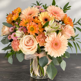 Peach and orange mixed bouquet in a clear glass vase with a ribbon