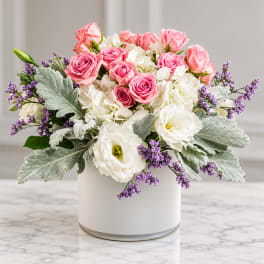 Pink roses and white blooms arranged in a white vase with purple accents