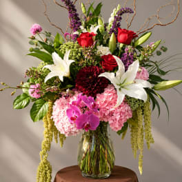 Large mixed bouquet with red roses, white lilies, pink hydrangeas, and orchids in a glass vase