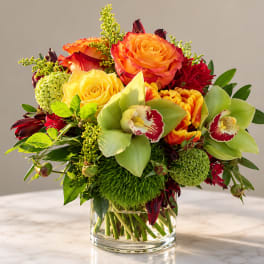 Mixed bouquet of orange and yellow roses with green orchids in a glass vase